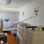 Children's bedroom with Bedroominabox-5-in-1Cot white crib, dresser, and toys on a wooden floor.
