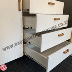 White drawers with wooden handles on a black floor, featuring a website URL.