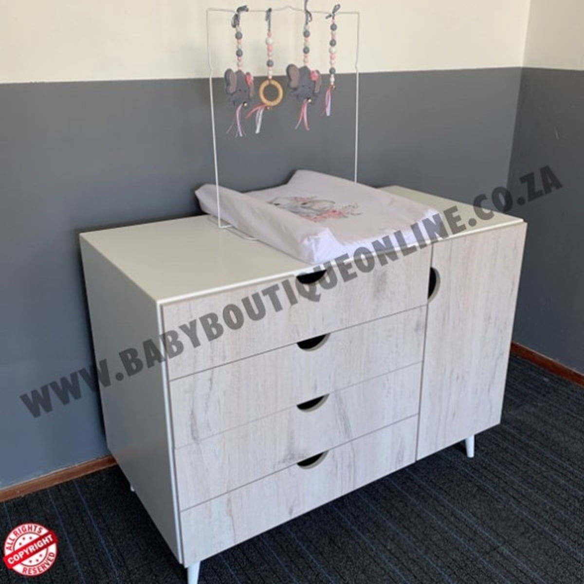 Wooden dresser with baby items against a gray wall, featuring 'www.babyboutiqueonline.co.za' branding.