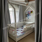 Children's room with a white crib and colorful bedding, curtains, and ceiling fan.