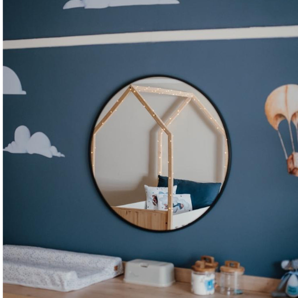 Tent Large Cot-White_OakSmoke Round mirror with house-shaped frame on a blue wall with cloud and hot air balloon decorations.