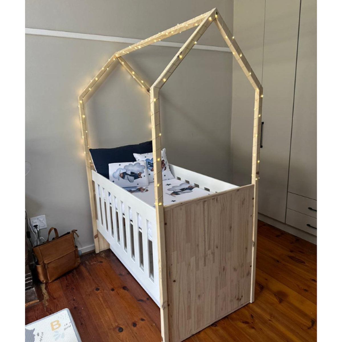 Tent Large Cot-White_OakSmoke with a house-shaped top and string lights, placed in a room with wooden flooring and a wardrobe.