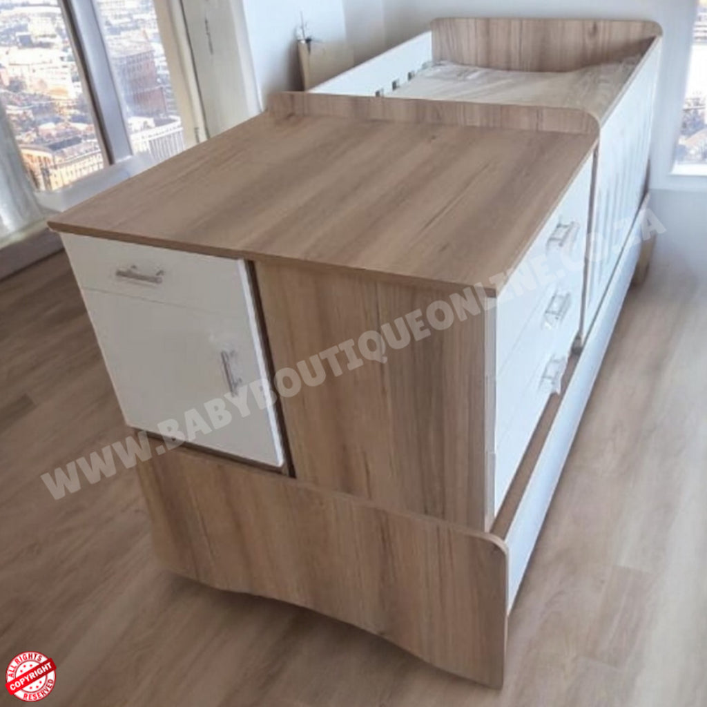 Wooden BabyBedroominaBox-5-in-1Cot with pull-out desk in a room with large windows.