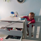 Child playing with a toy in a BabyBedroominaBox5-in-1Cot crib next to a white dresser with open drawers.