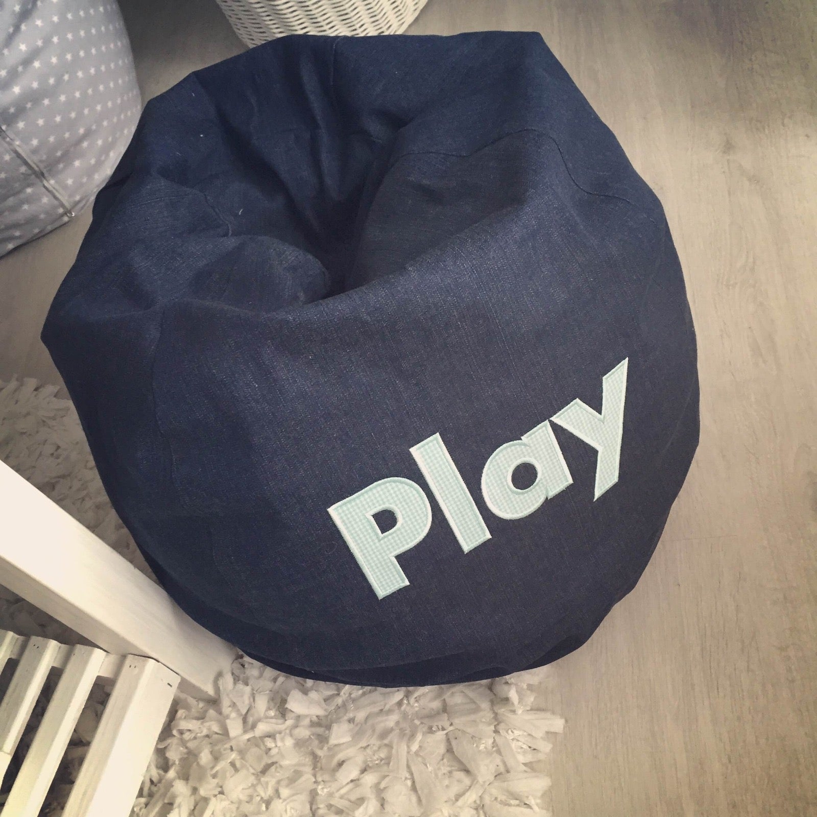 Navy bean bag chair with 'Play' text on a wooden floor.