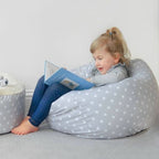 Child sitting on a star-patterned bean bag reading a book in a cozy room.