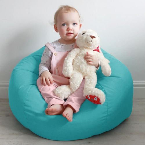 Child sitting on a turquoise bean bag holding a teddy bear against a white background