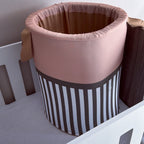 A fabric baby crib basket tan, and brown, featuring vertical brown and white stripes on the lower half, shown inside a white crib.