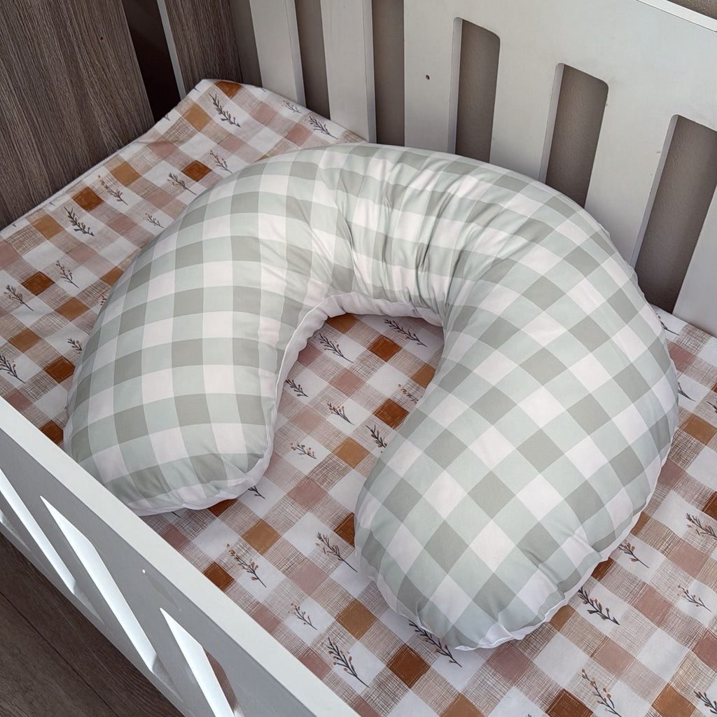 Green and white checkered U-shaped pillow on a crib with a patterned sheet.