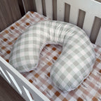 Green and white checkered U-shaped pillow on a crib with a patterned sheet.