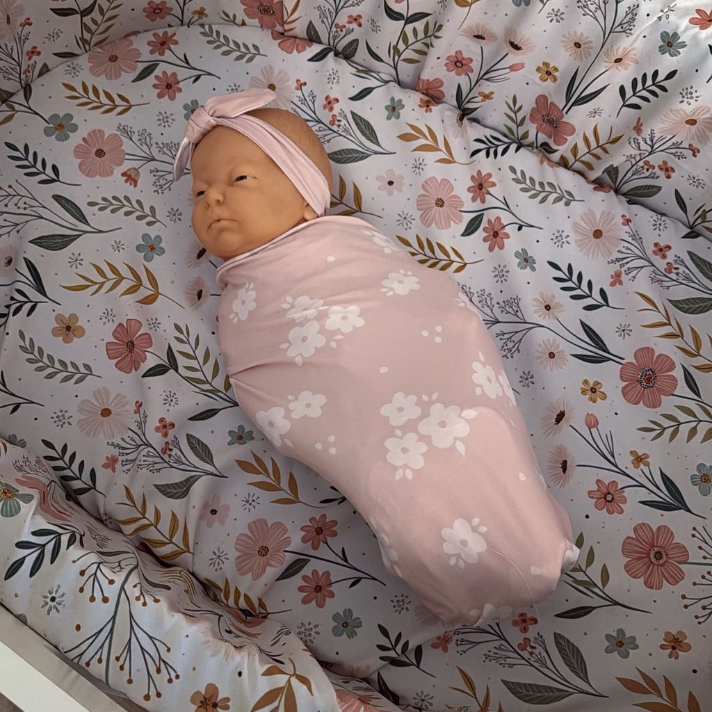 Newborn baby wrapped in a floral blanket on a floral crib sheet