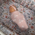Newborn baby wrapped in a floral blanket on a floral crib sheet