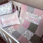A pink and white patchwork baby bedding set in a white crib, featuring a quilt with floral and gingham patterns, a matching pillow, and a personalized name pillow that reads 'Amariah'.