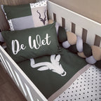 Crib with green bedding featuring a deer design and 'De Wet' text, surrounded by decorative elements.