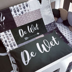 Patchwork blanket and pillow with 'De Wet' branding on a bed.