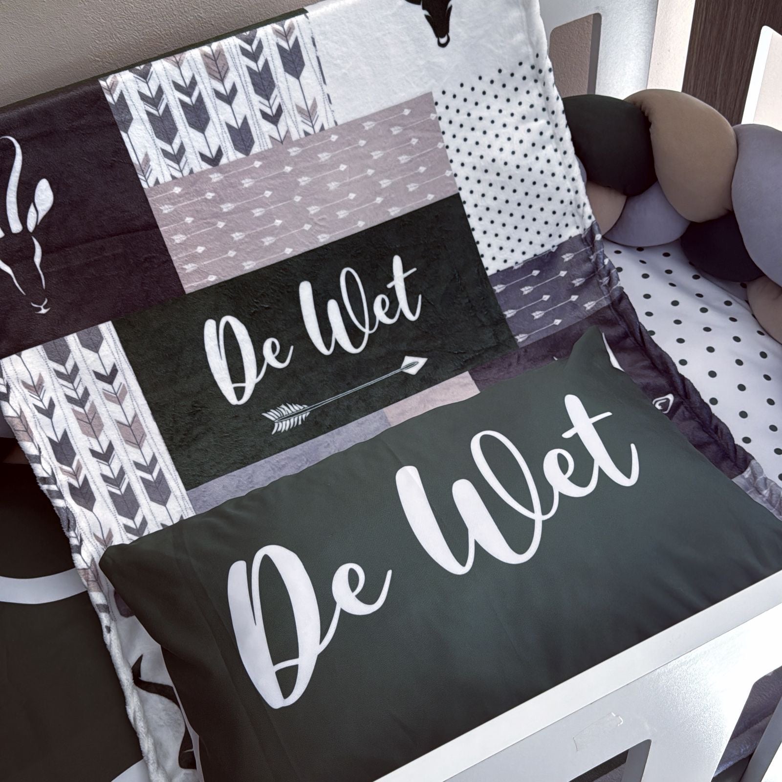 Patchwork blanket and pillow with 'De Wet' branding on a bed.