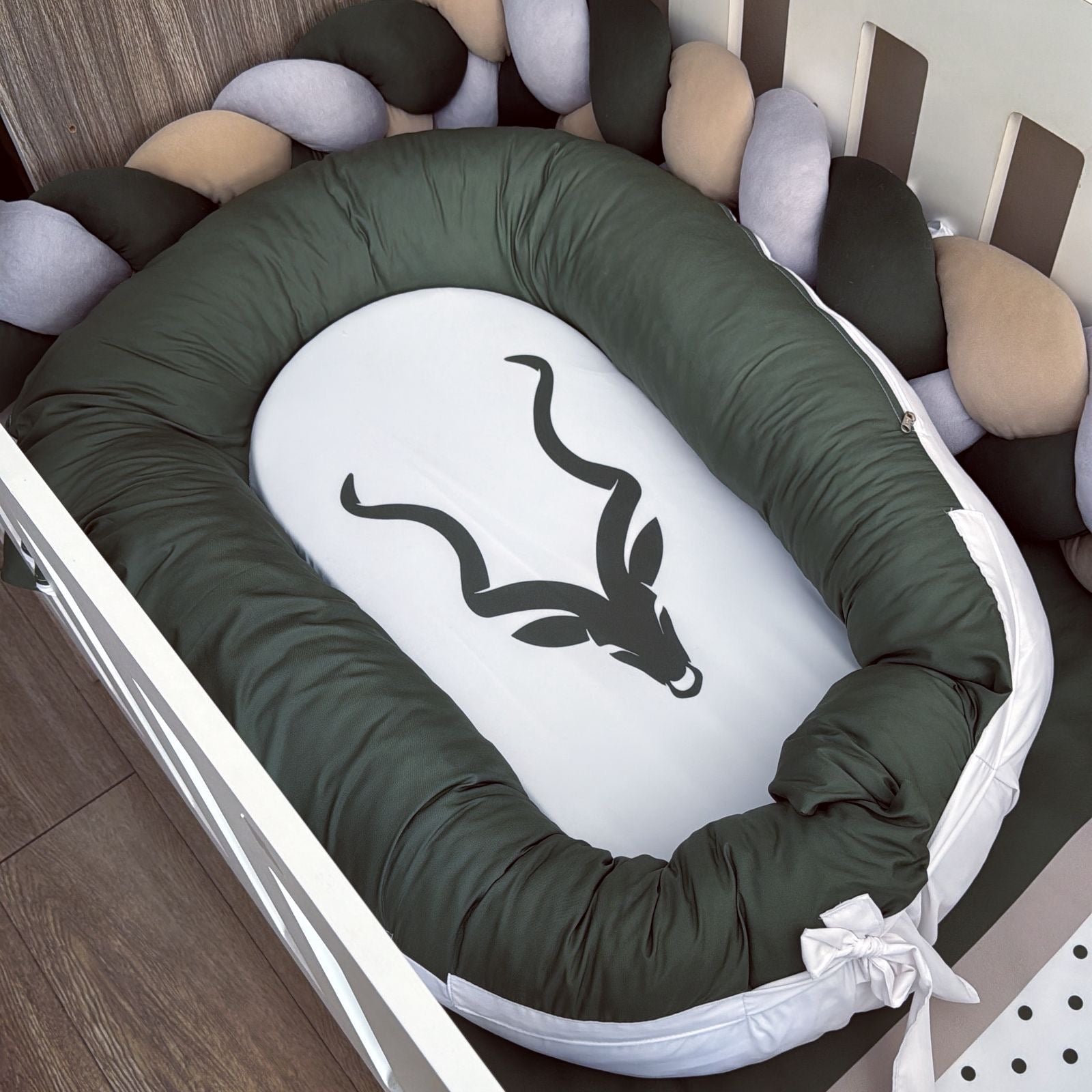 Baby crib with green bumper and white mattress featuring a black antelope design.