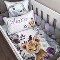 Customizable baby bedding set in a white crib, featuring a watercolor print of an elephant, zebra, lion cub, and purple flowers. Includes a white crib bumper with lavender and gray beads, a personalized pillow reading 'Anita' in purple script, and a matching elephant pillow.