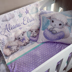 A baby bedding set in a white crib, featuring a blanket and matching pillow with cute cartoon sheep illustrations, purple accents, and the personalized name 'Aliana-Ebria' in purple script.