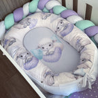 A baby bassinet bedding set featuring a padded bassinet cover with a white background and a lavender and gray lamb pattern, a matching oval insert with a central lamb illustration, and a braided crib bumper in pastel purple, mint green, and white.