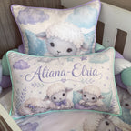 Personalized baby bedding set featuring two plush throw pillows in a nursery crib. The front pillow is personalized with the name 'Aliana-Elria' in purple script, and the back pillow shows a cute cartoon lamb.