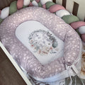 Floral-patterned baby crib bumper with decorative pillow on a wooden floor.