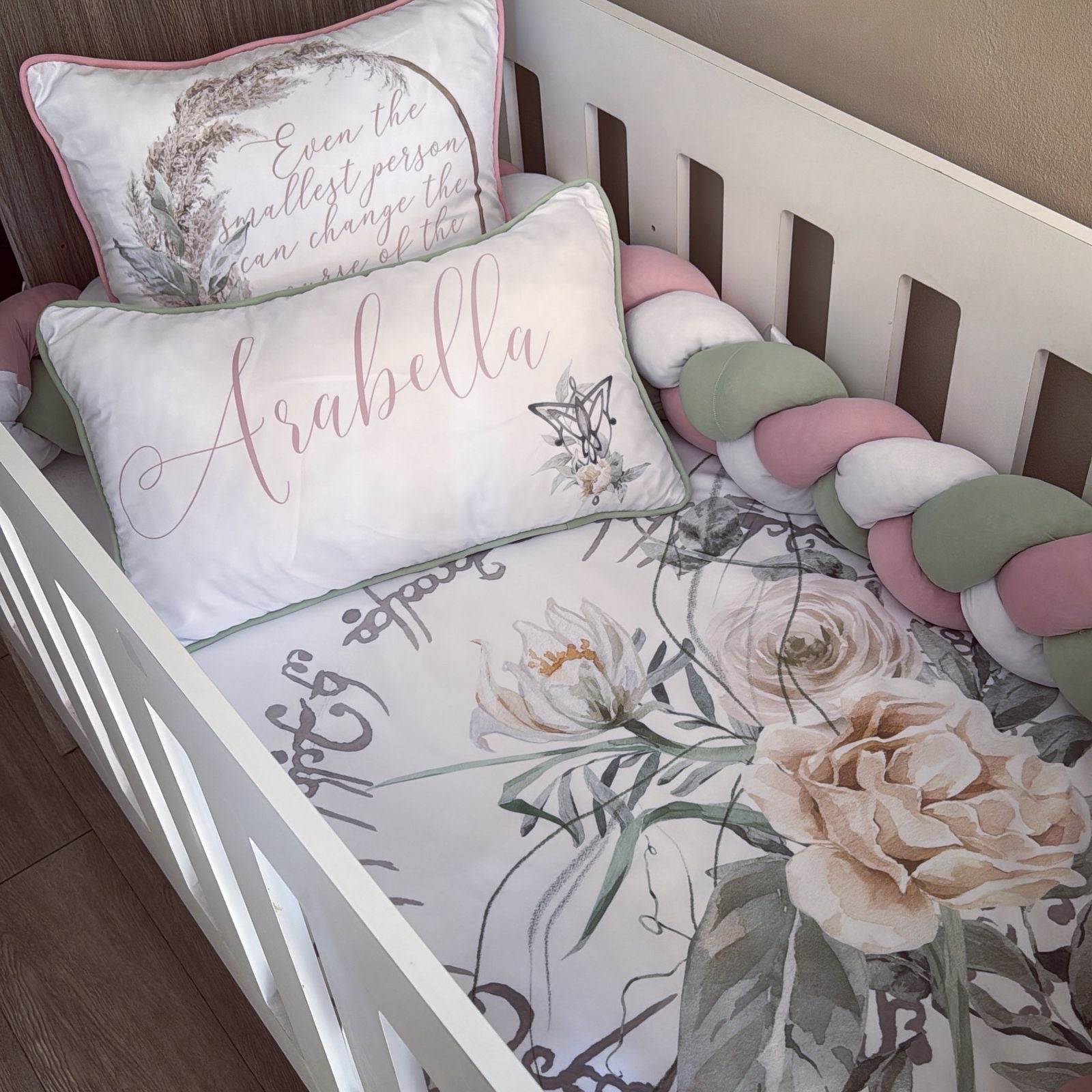 Crib with floral bedding, decorative pillow, and colorful bumper