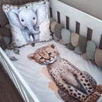 A white crib with a watercolor print bedding set featuring a cheetah cub on the mattress and a matching elephant pillow, surrounded by a multi-colored chunky bumper.