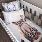 A baby crib bedding set featuring a printed cheetah on the fitted sheet and matching elephant pillowcase, styled inside a white wooden crib with a soft cushion bumper.