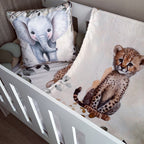 A baby bedding set in a white crib, featuring a cream-colored blanket with a watercolor cheetah print and a matching elephant pillow.