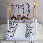 A baby changing pad with a wooden hanging toy bar, featuring colorful animal and rainbow toys, displayed on a white dresser against a neutral gray wall.