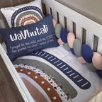 A styled nursery crib setup featuring a personalized navy blue pillow with white text reading 'waVutali I prayed for this child, and the LORD has granted me what I asked of him', a matching printed bumper cushion, and a chunky braided crib bumper in navy, blush pink, and gray.