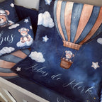 A cozy children's bedding set featuring a dark blue space-themed blanket and matching pillows with a watercolor hot air balloon, teddy bear, clouds, stars, and the personalized name 'Købus de Klerk' in white script.