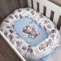 A baby crib bedding set featuring a white bassinet bumper pad with a brown teddy bear and airplane pattern, surrounding a light blue oval mattress topper with a matching teddy bear illustration.