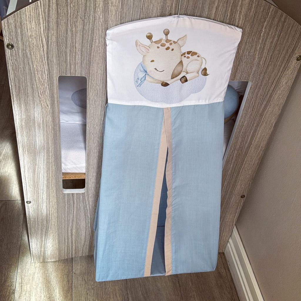 Baby crib with a blue sheet and a pillow with a giraffe design in a wooden crib.