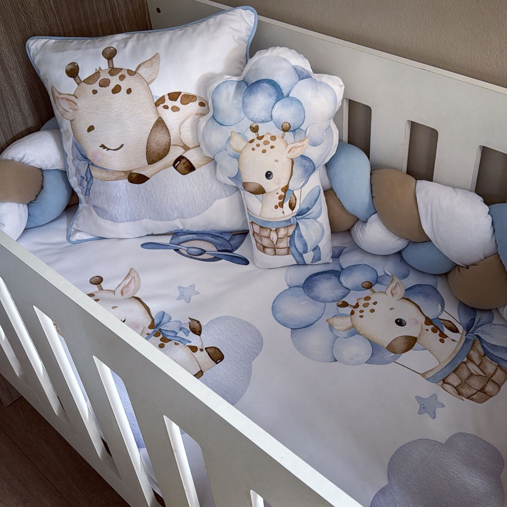 Baby crib with blue and brown giraffe-themed bedding and pillows.