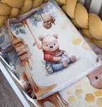 Baby crib sheet with cartoon bear and honey design, surrounded by yellow plush toys.