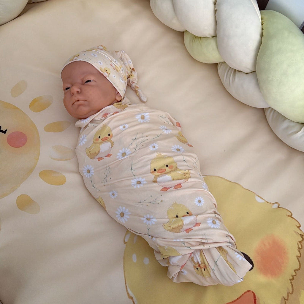 Newborn baby swaddled in a blanket with duck patterns on a soft surface.