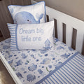 A blue and white baby bedding set styled in a white wooden crib, featuring a duvet cover with a playful sea-creature print, a striped pillow, and a whale-print pillow.