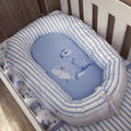 A baby bassinet cushion set with a light blue and white striped fabric border and a matching blue insert featuring a shark and whale illustration, shown inside a white crib.