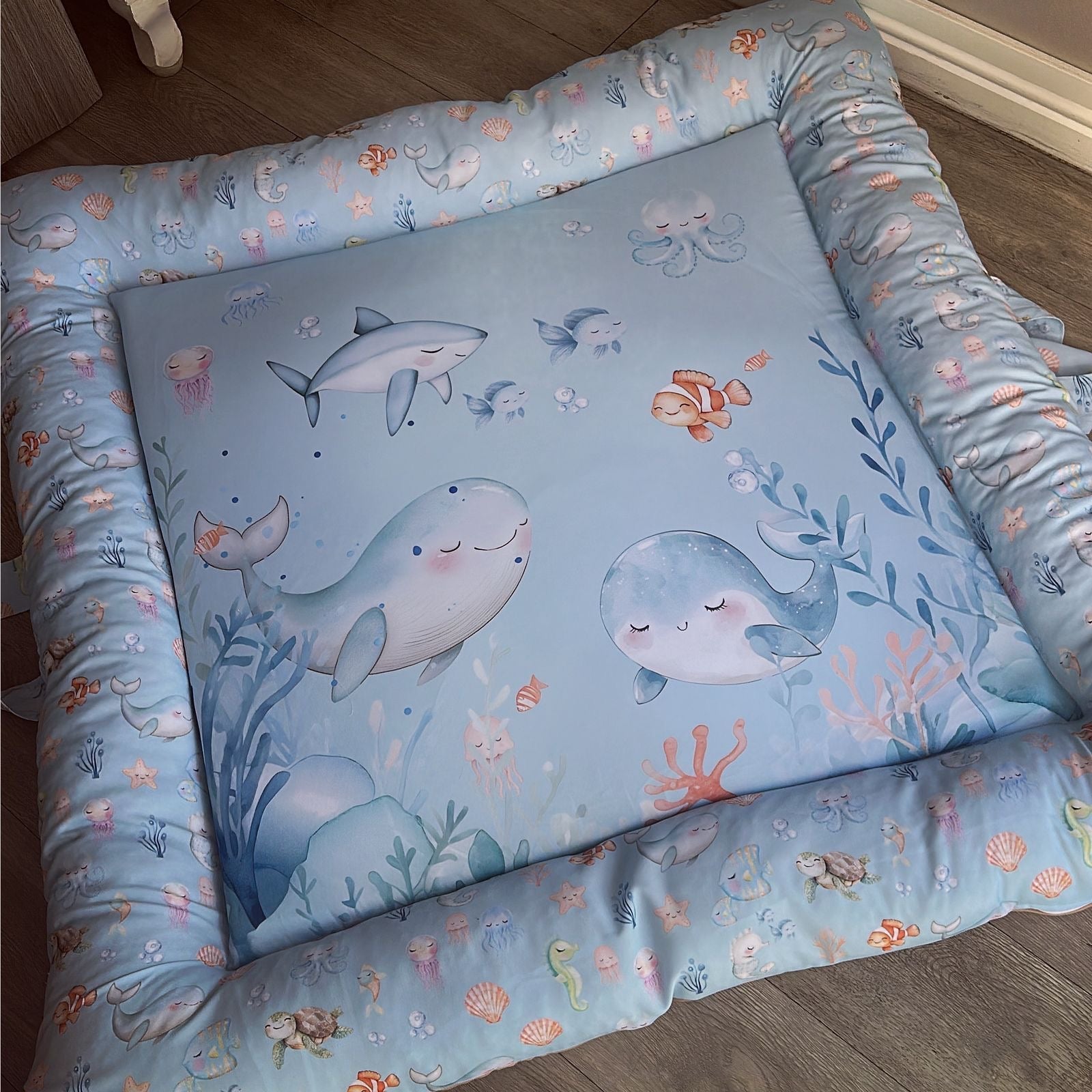 Baby doughnut with blue sheet featuring whale illustrations on a wooden floor.