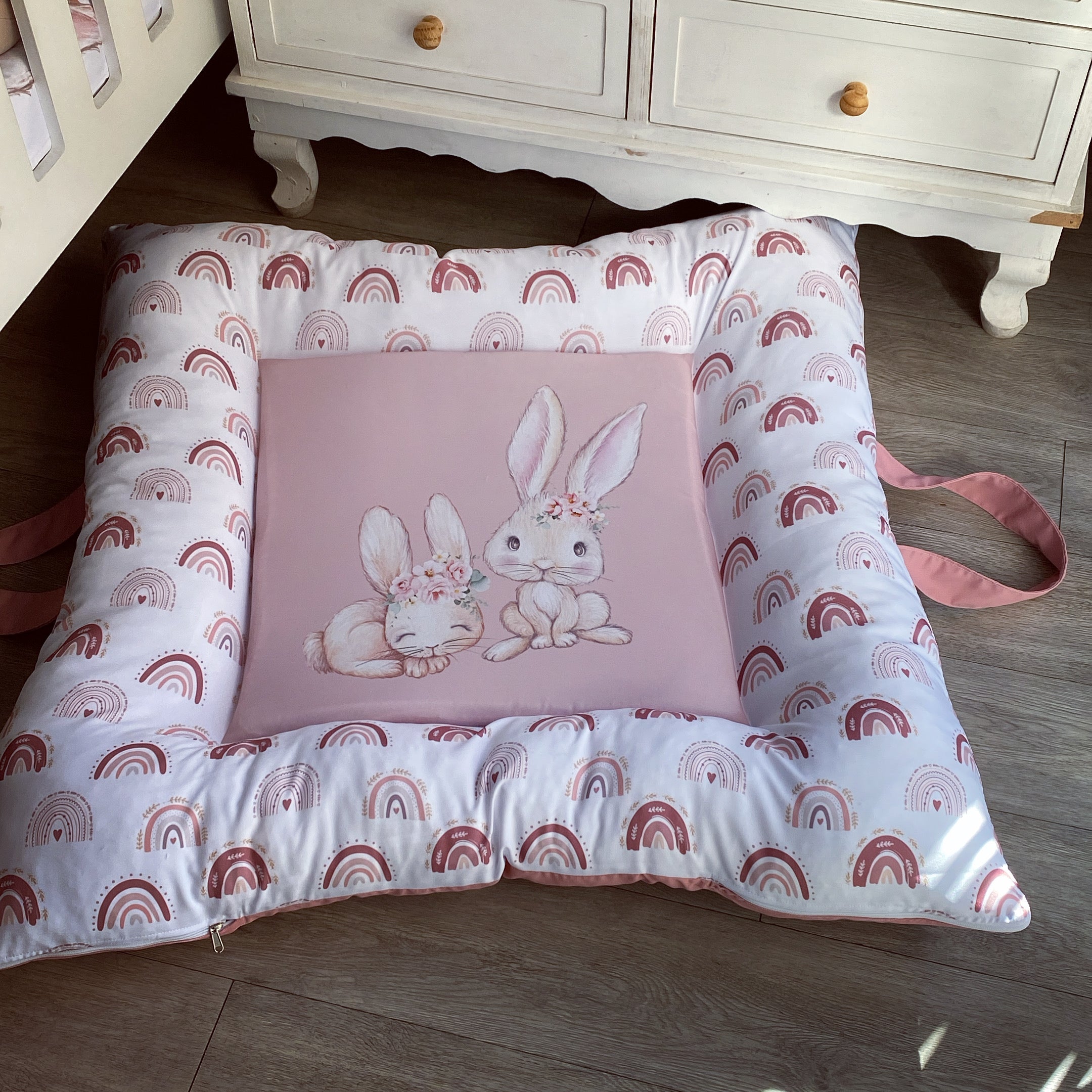 A soft play doughnut for babies with a pink center featuring a cute character, surrounded by a pattern of rainbows and bunnies in a grey and blue color scheme.
