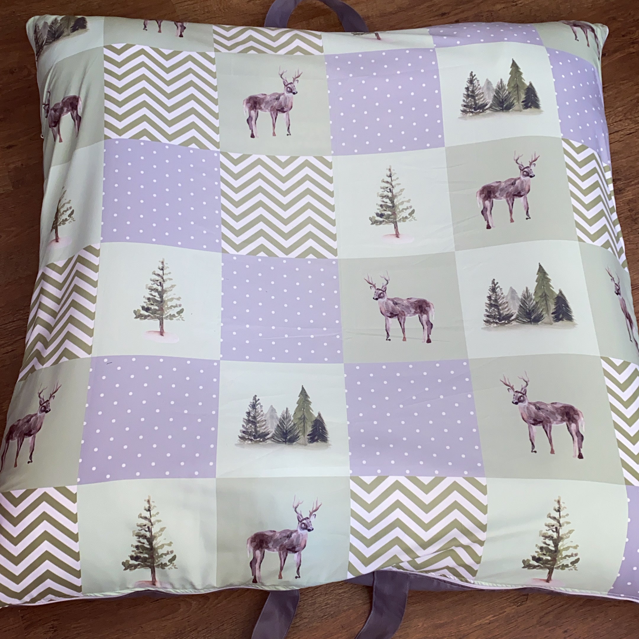 Patchwork pillow with deer and tree patterns on a wooden surface