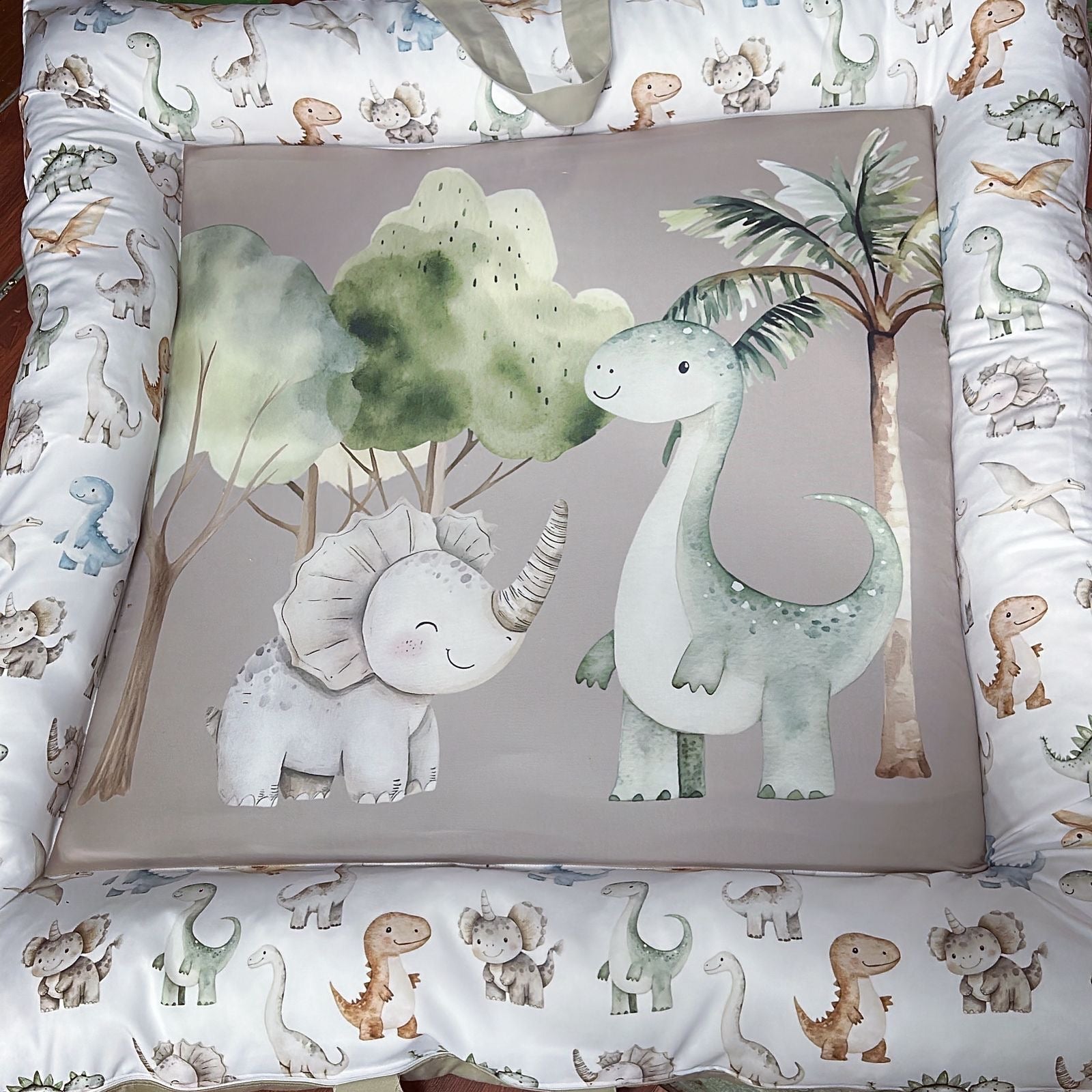 Baby crib bumper with dinosaur illustrations on a patterned background