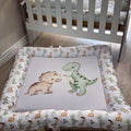 Baby crib with dinosaur-themed bedding and mattress pad in a nursery setting.
