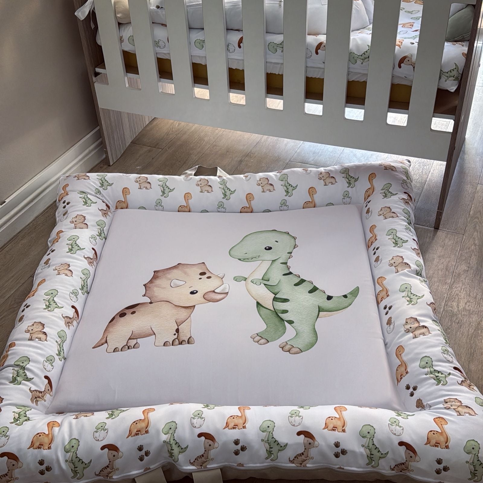 Baby crib with dinosaur-themed bedding and mattress pad in a nursery setting.