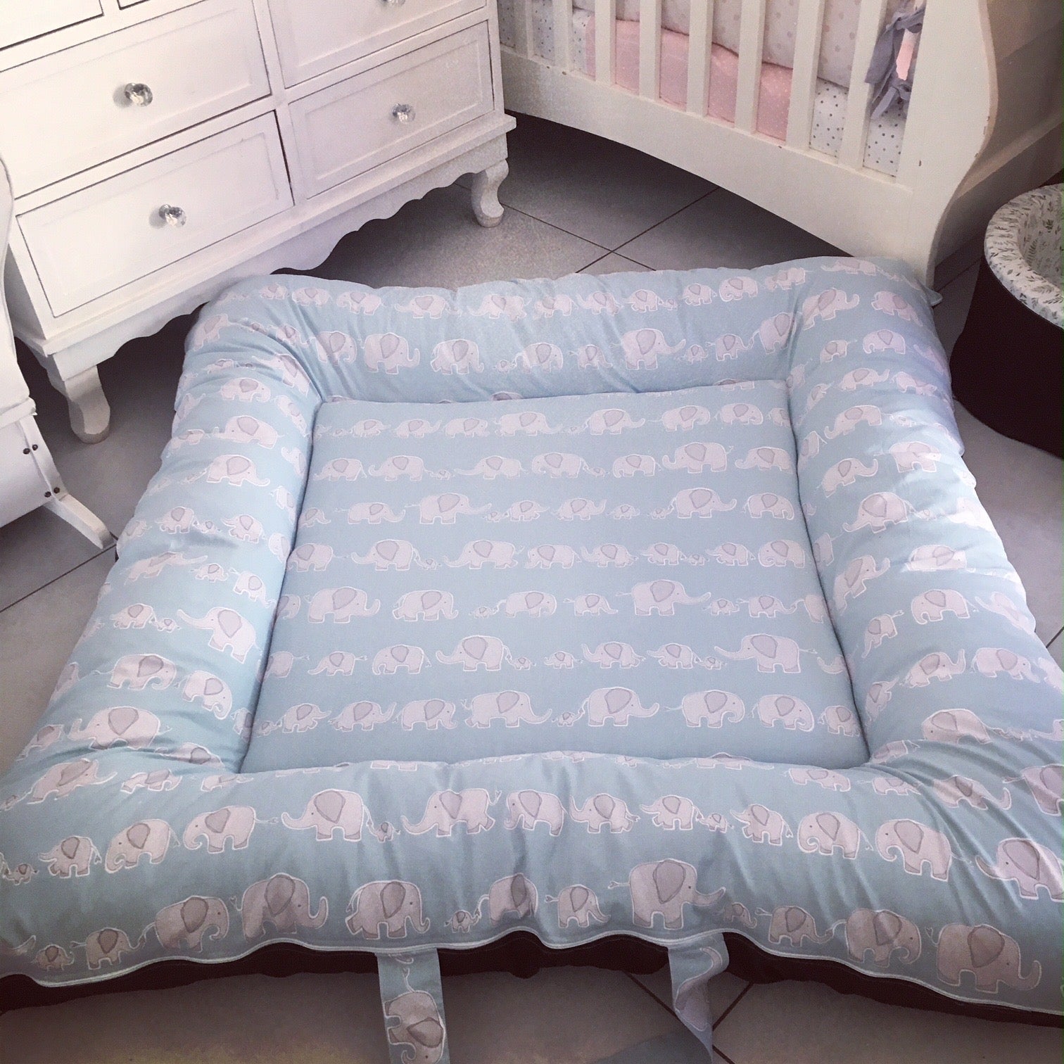 Blue baby crib bumper with elephant pattern in a nursery setting