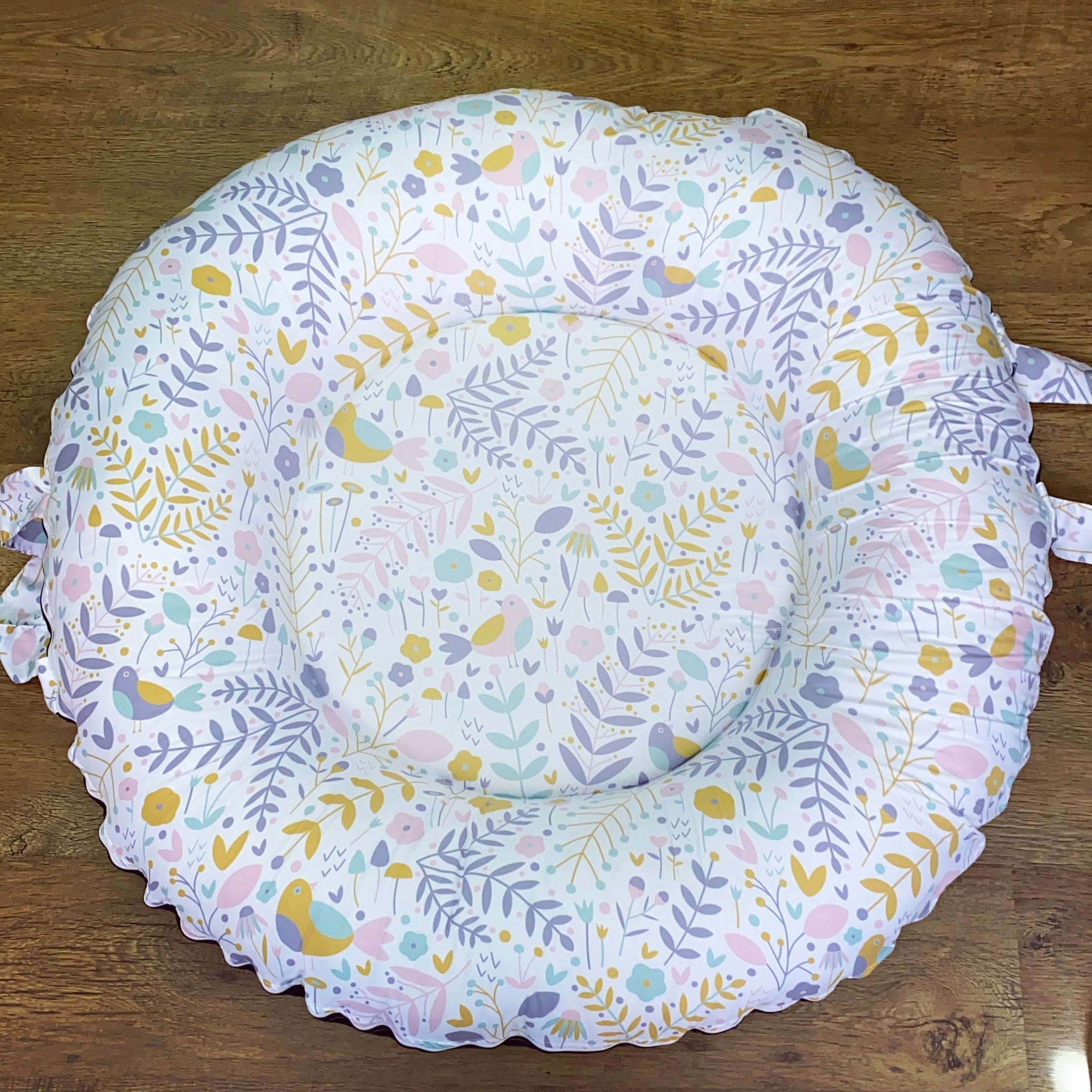 Round baby play mat with floral and bird pattern on a wooden floor