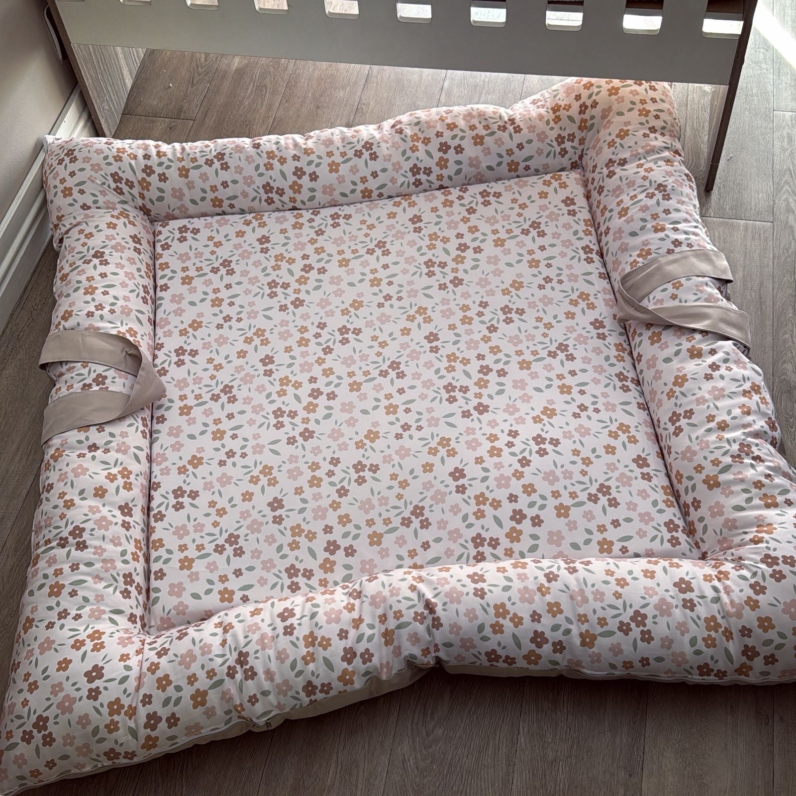 Floral-patterned crib bumper on a wooden floor