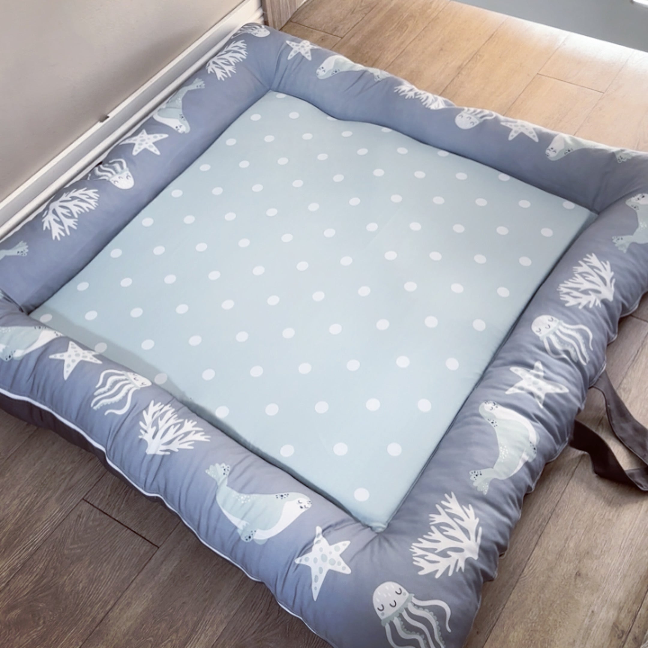 A gray baby play doughnut with a washable cover, featuring a pattern of sea creatures and stars on a light blue background.